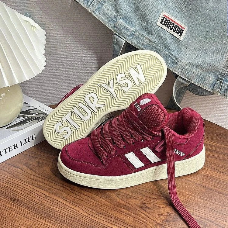 Burgundy sneakers with white side stripes, wide laces and one cream-colored outsole facing upward