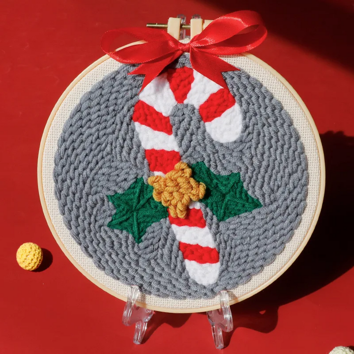 Candy cane punch needle hoop with red and white stripes, green holly, and a gray background
