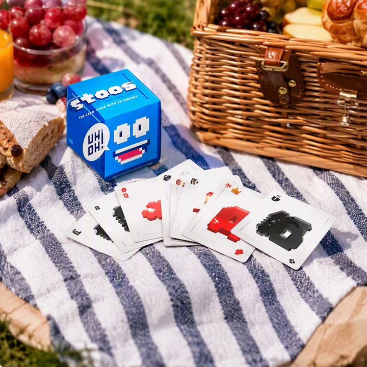 Blue card game box and illustrated cards on a picnic blanket beside a basket
