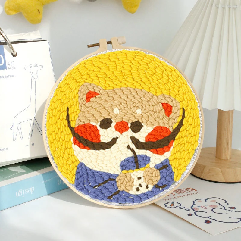 Cartoon cat punch needle hoop with rosy cheeks, a blue bow, and a bright yellow background