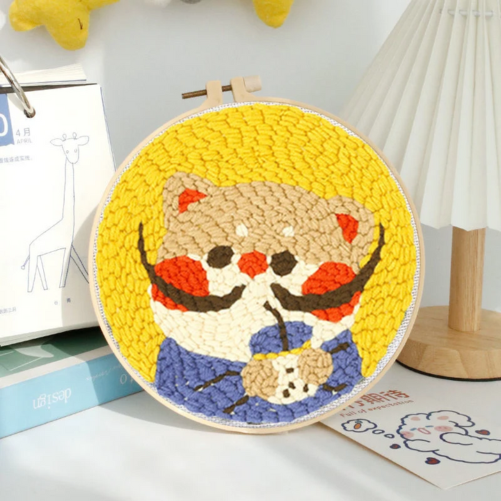 Cartoon cat punch needle hoop with rosy cheeks, a blue bow, and a bright yellow background