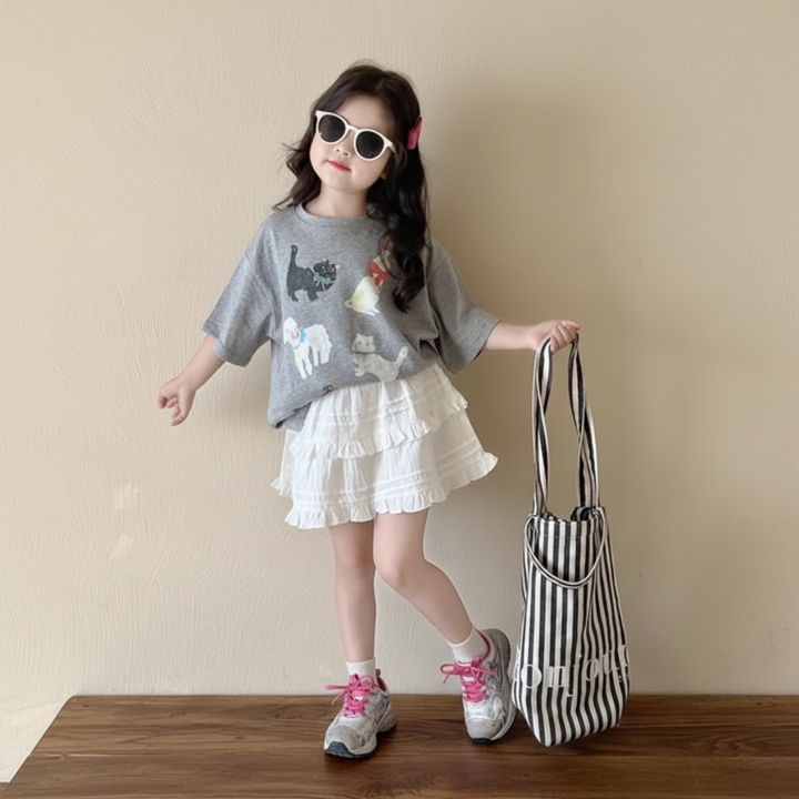 Gray cat-print tee partly tucked into a white ruffled skirt, worn with sunglasses and sneakers.