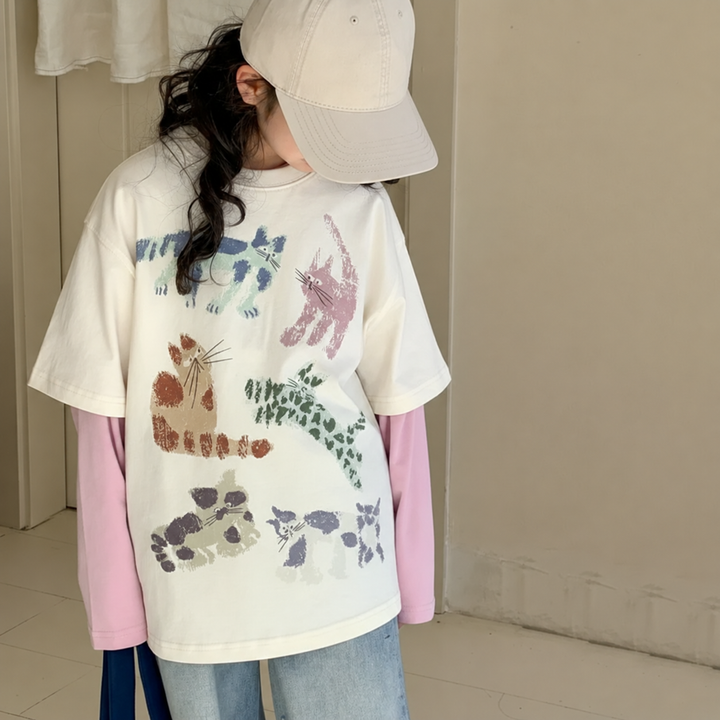 Front view of a girl wearing the cream cat-print top with pink sleeves and jeans