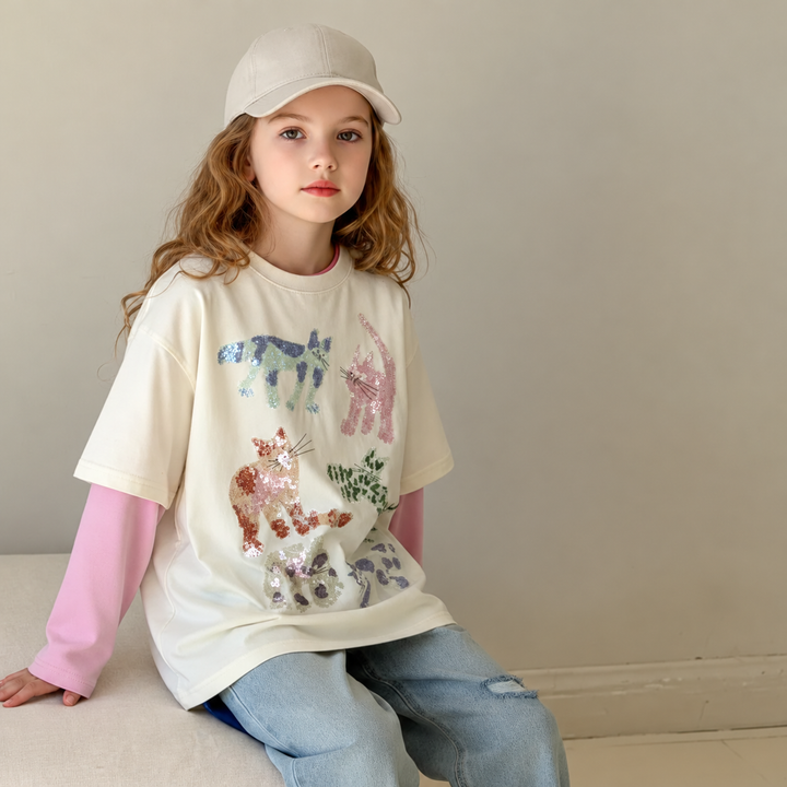 Seated girl wearing the cat-print layered-look top with jeans and a beige cap