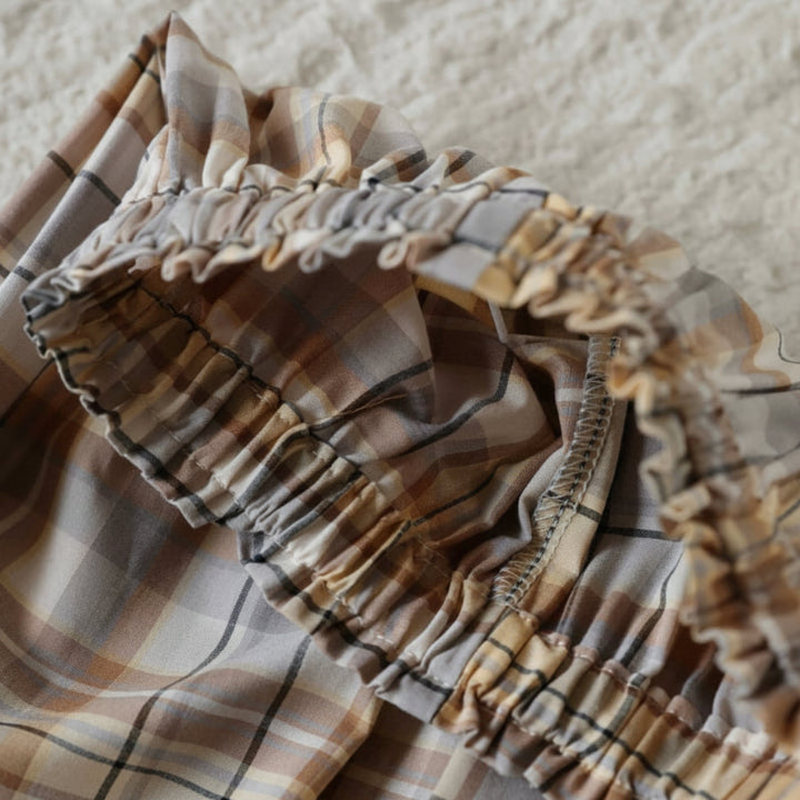 Close-up of the ruffled elastic waistband on beige and brown checkered pants.