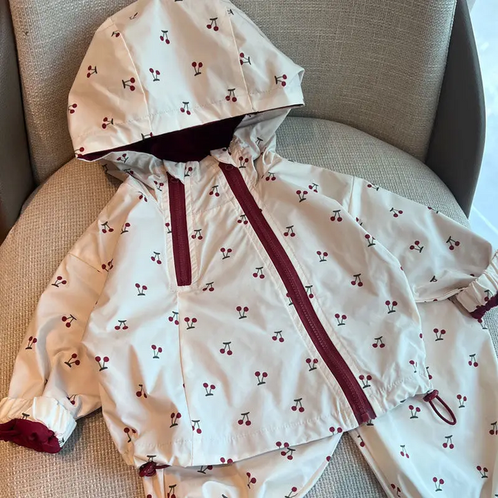 Cherry-print hooded jacket with a burgundy zipper and elastic sleeve cuffs on a gray chair.