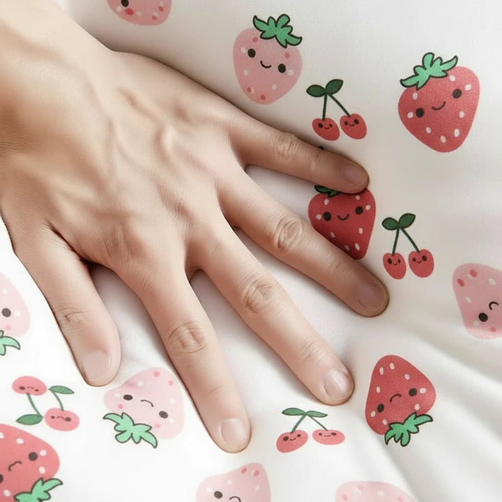 Hand resting on white swaddle fabric patterned with cherries and strawberries