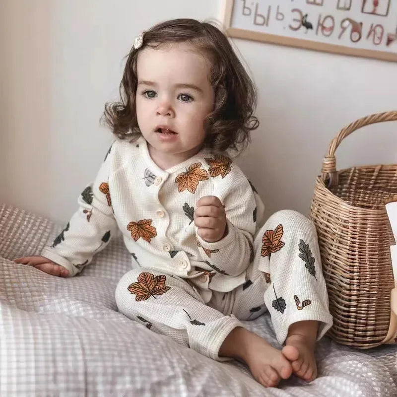 Child seated on a bed wearing a white long-sleeve pajama set with colorful leaf prints