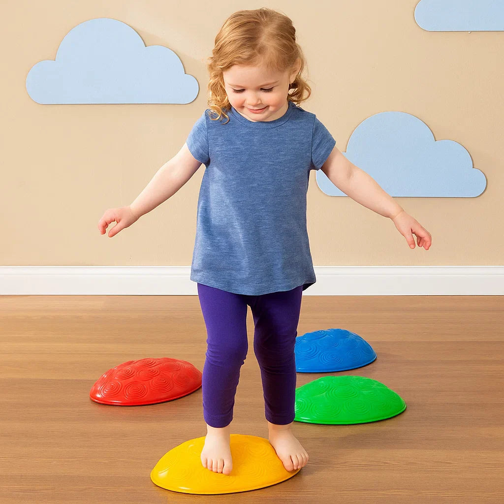 Child balancing on a yellow stepping stone with red, blue, and green stones nearby