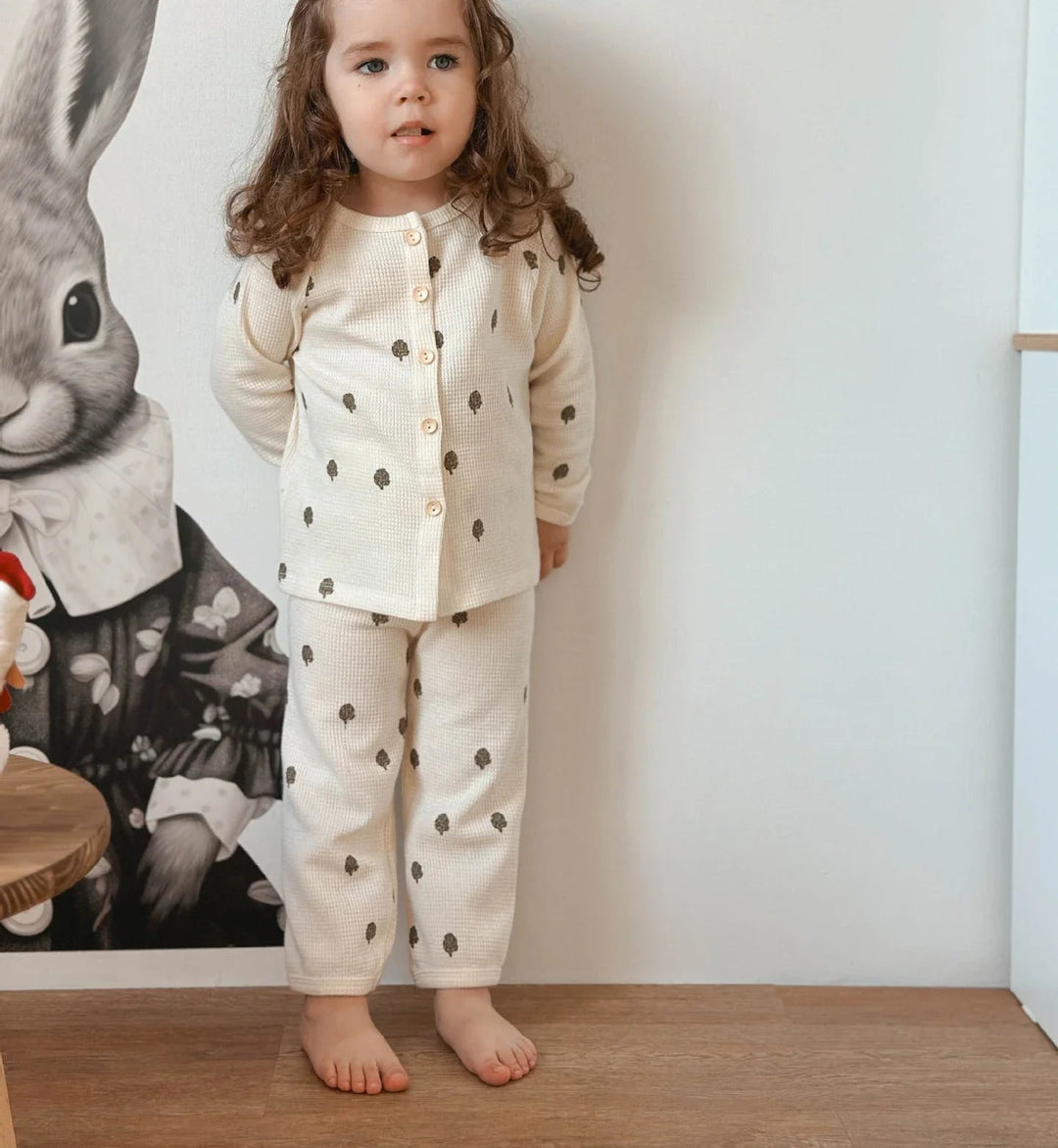 Child standing in a beige fruit-print pajama set with a button-front top