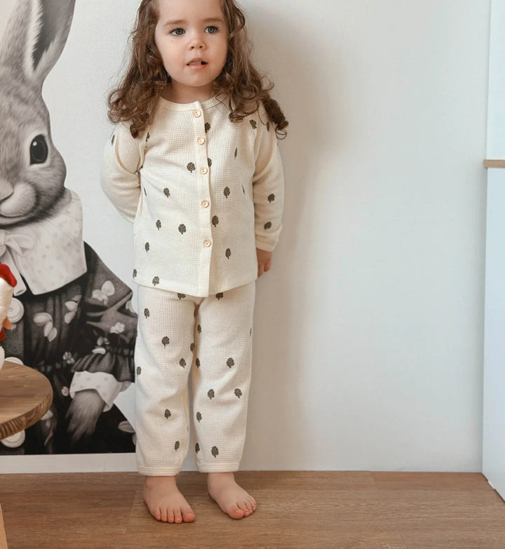 Child standing in a beige fruit-print pajama set with a button-front top
