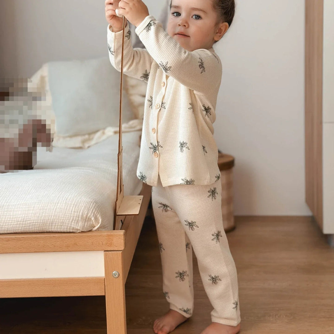 Child wearing beige insect-print cotton pajamas while standing beside a bed