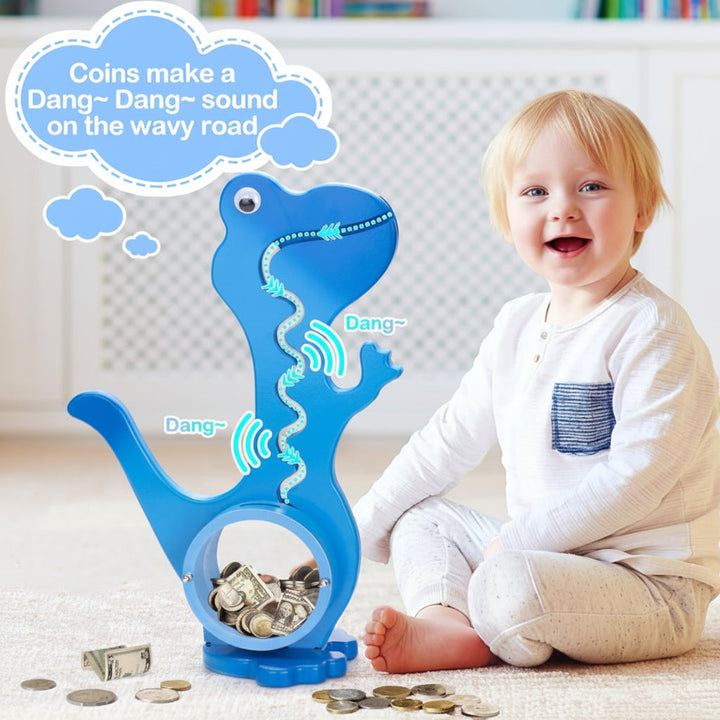 Child sitting beside a blue dinosaur piggy bank with coins and bills on the floor