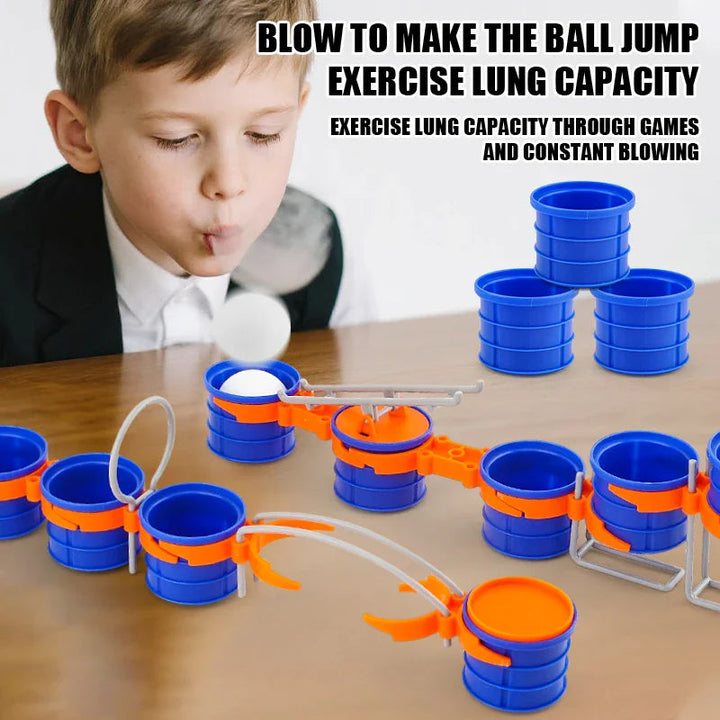 Child blowing a white ball along a tabletop course of blue cups, orange connectors and gray obstacles