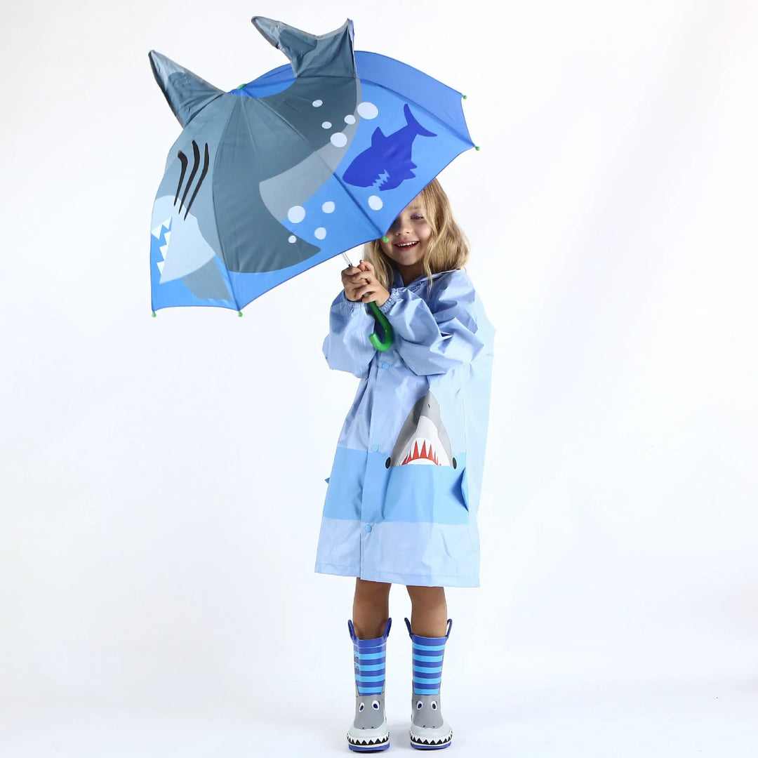 Child holding a blue shark umbrella while wearing a blue raincoat