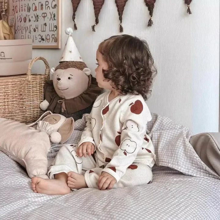 Child sitting on a bed in white cotton pajamas with brown apple prints
