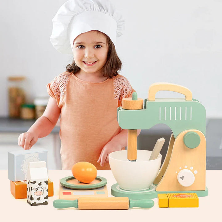 Child in a chef hat beside a green wooden mixer play set and pretend baking ingredients