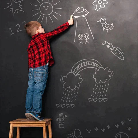 Child adding chalk drawings to a wall covered in black chalkboard wallpaper