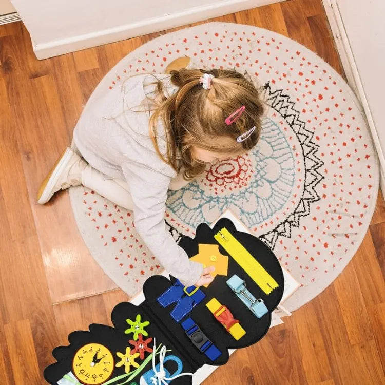 Child exploring the fastenings on an open dinosaur busy board on the floor.