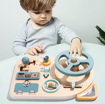 Child exploring the steering wheel and controls on a wooden driving activity board