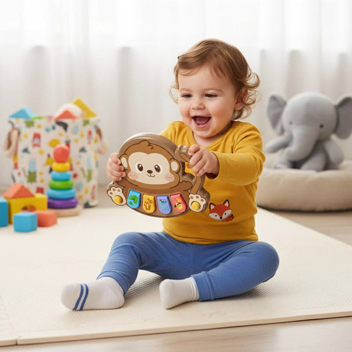 Child seated on a play mat holding a brown monkey animal piano