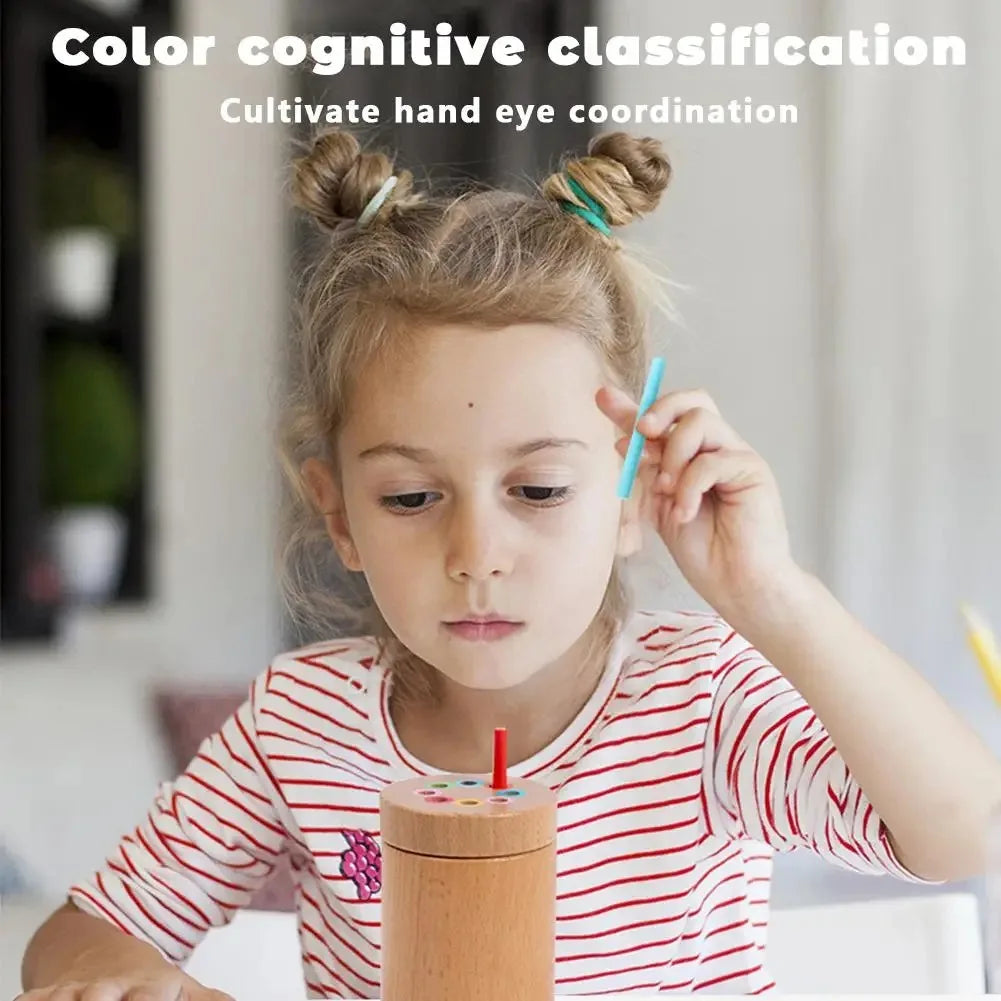 Child holding a blue stick beside a wooden color sorter with a red stick in the lid.