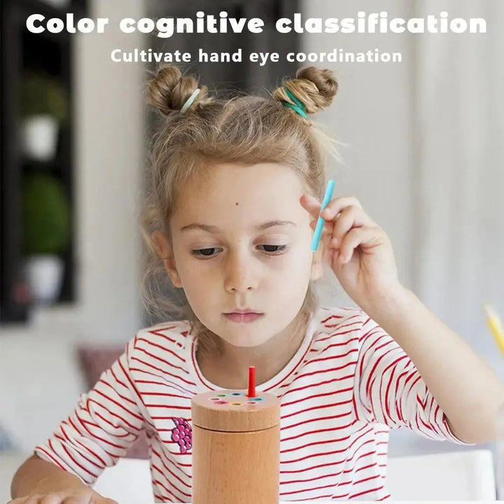 Child holding a blue stick beside a wooden color sorter with a red stick in the lid.