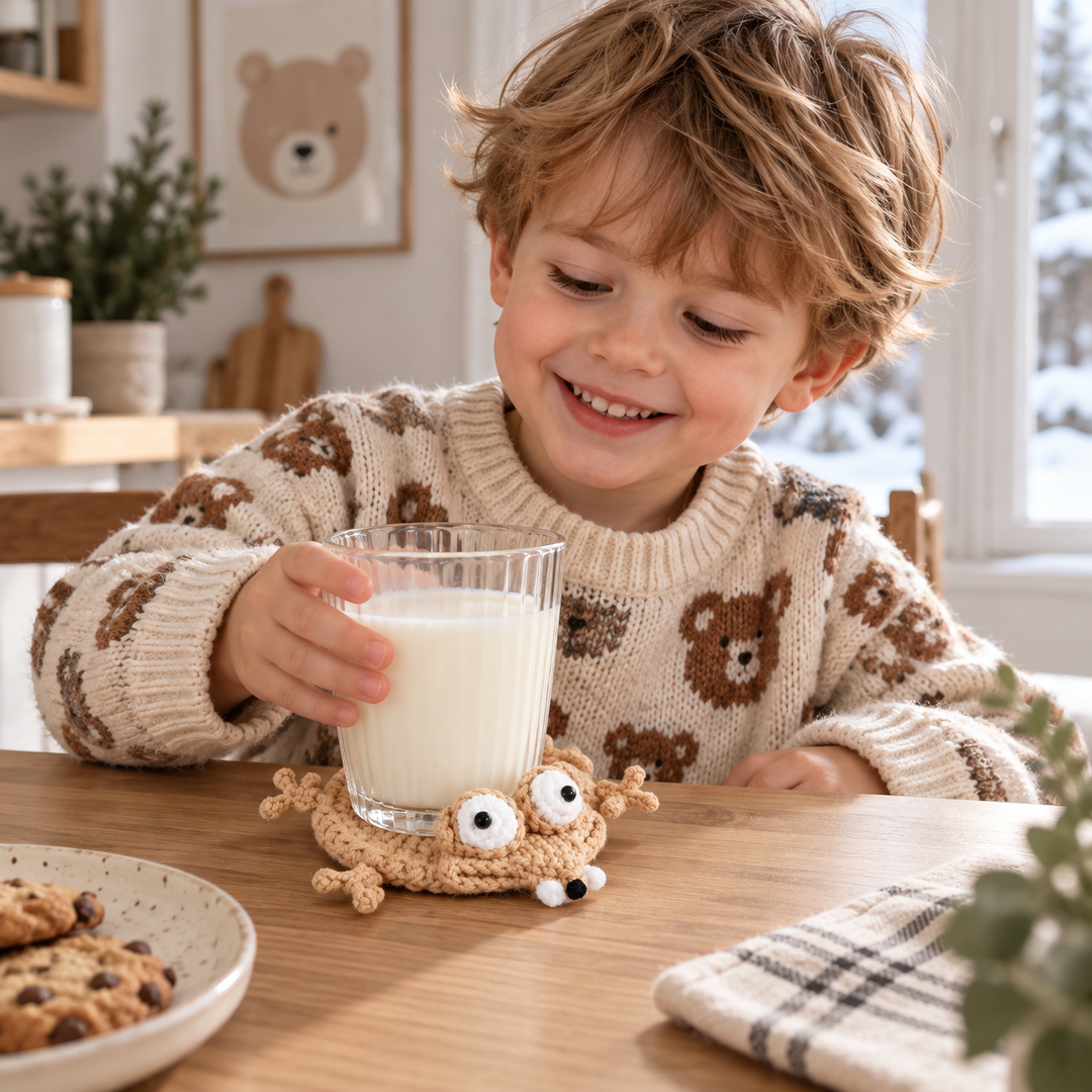 Child holding a glass of milk on a beige crocheted animal coaster at a wooden table
