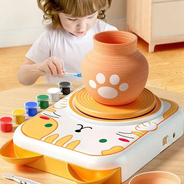 Child painting a clay vase with a paw-print design on the cat-themed pottery wheel