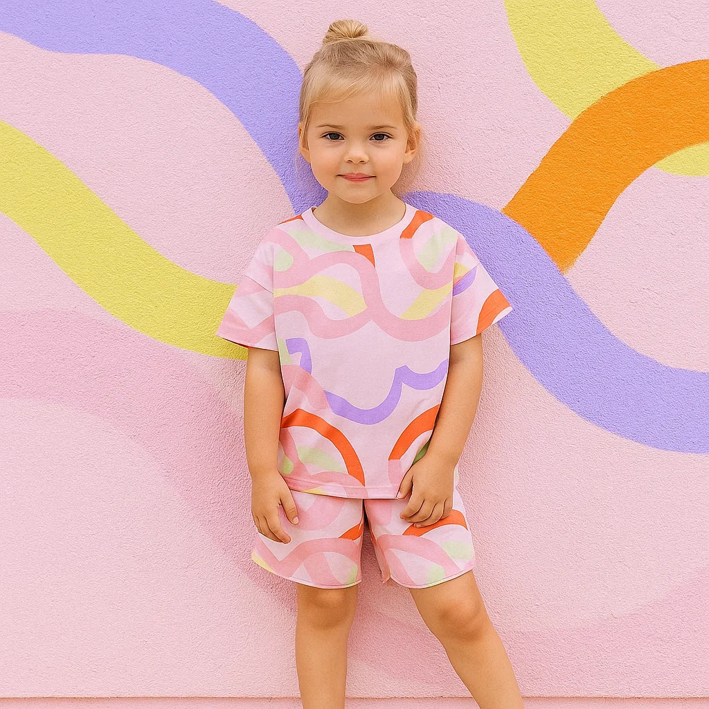 Child wearing a pink multicolor swirl top and shorts beside a colorful mural