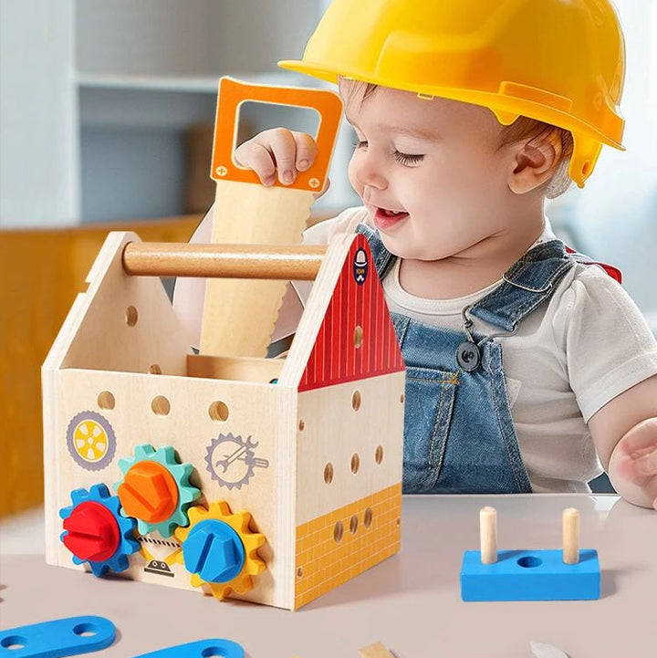Child in a yellow hard hat holding a toy saw beside a wooden activity box
