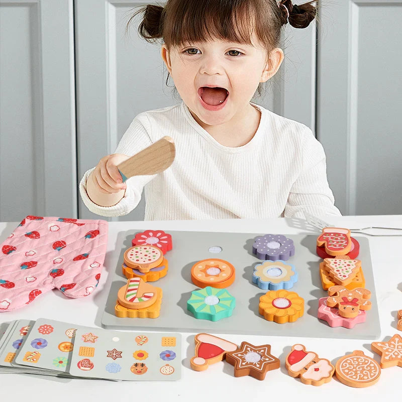 Child holding a toy knife beside a tray of wooden cookies, pattern cards, and a pink oven mitt.