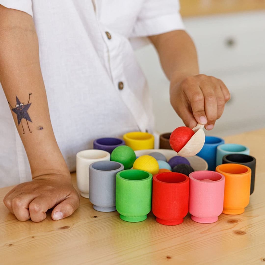 Child using a wooden spoon to lift a red ball from the color sorting set