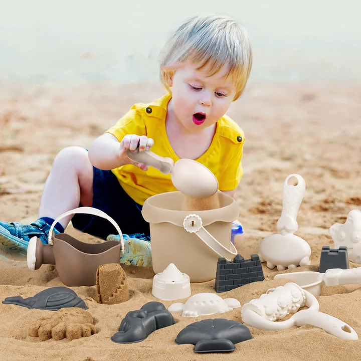 Child scooping sand into a beach bucket with tools and sand molds nearby