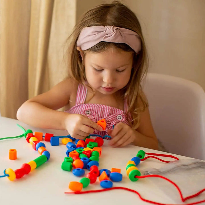 Child threading colorful beads at a table with additional beads and cords