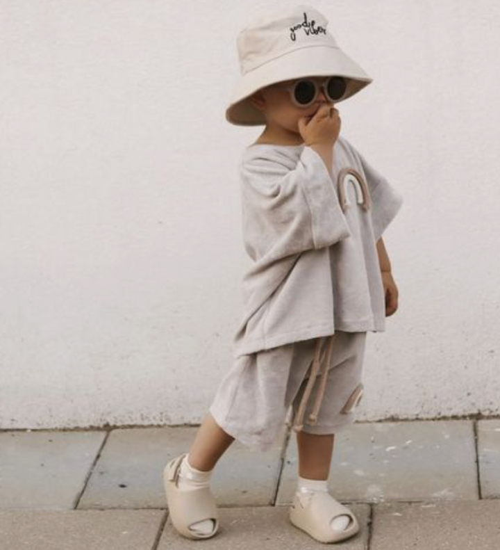 Child wearing beige sandals with a matching casual outfit and sun hat outdoors.