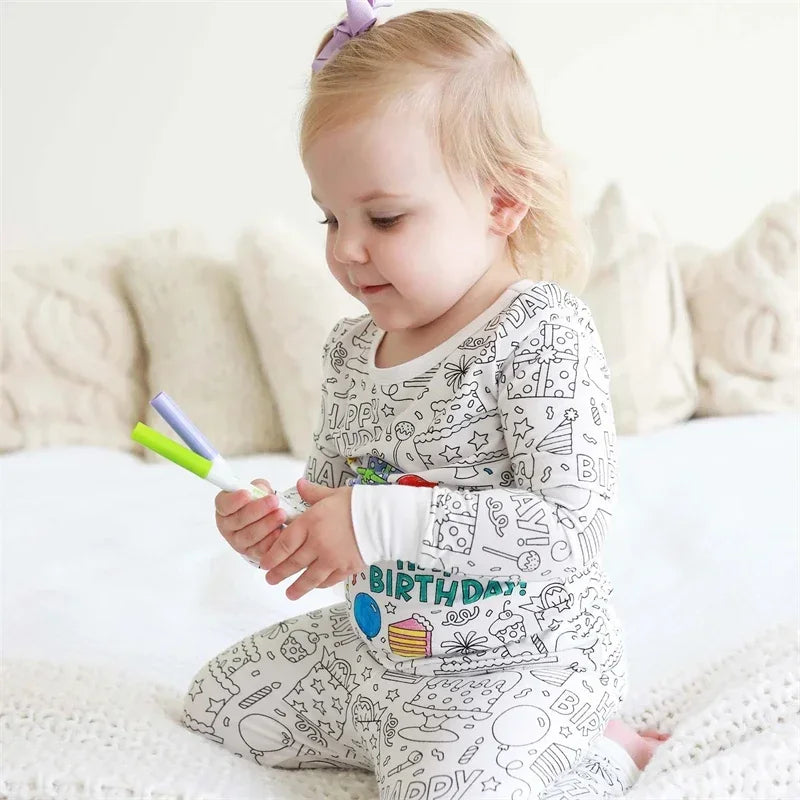 Child wearing partially colored birthday-print pajamas and holding markers