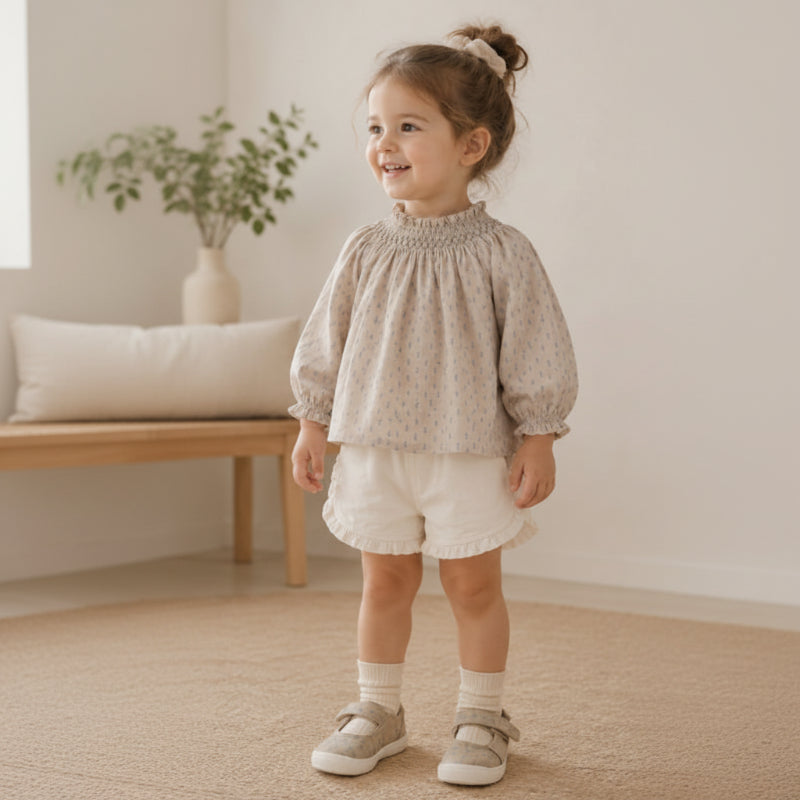 Child wearing a printed top with a gathered neckline and white ruffle-hem shorts