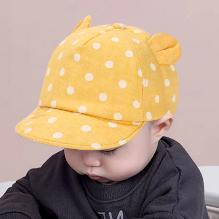 Child wearing a yellow cap with white polka dots and padded ears.