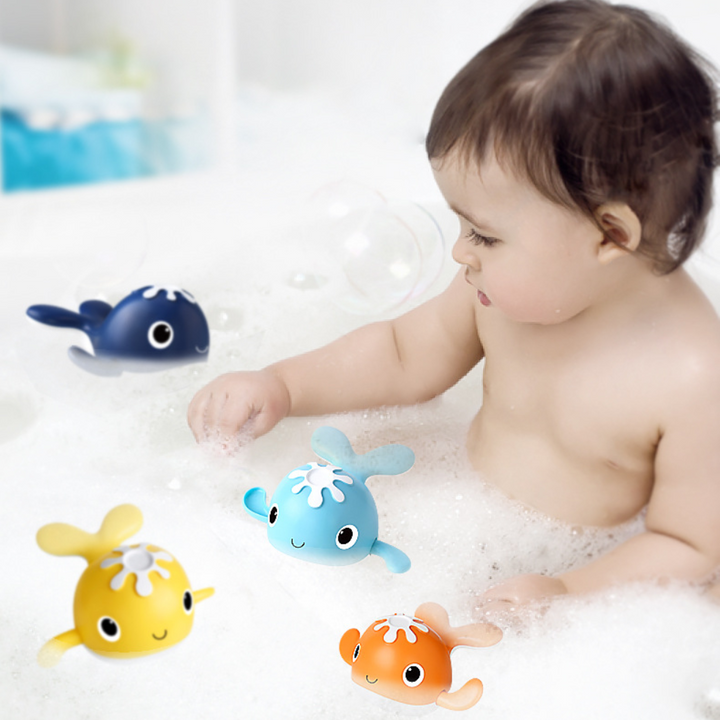 Child playing with yellow, orange, navy and light blue whale toys in a bubble bath.