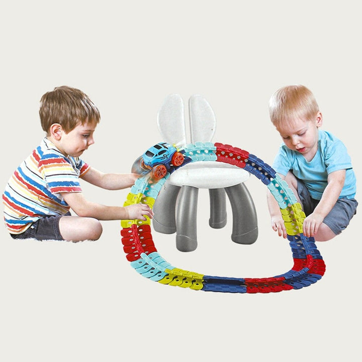Two children assembling a multicolor flexible race track around a small white chair