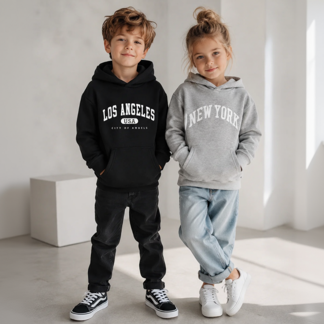 Two children wearing black Los Angeles and gray New York hoodies with pants and sneakers.