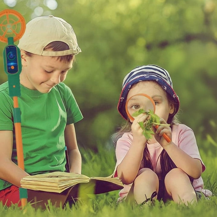 Two children exploring outdoors with a metal detector, magnifying glass, and open book