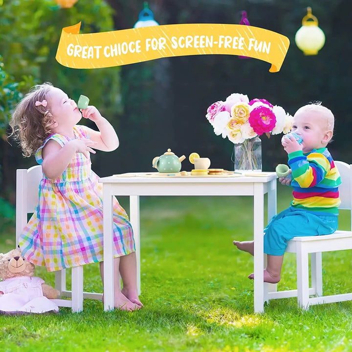 Two children having an outdoor tea party at a small table with a wooden tea set