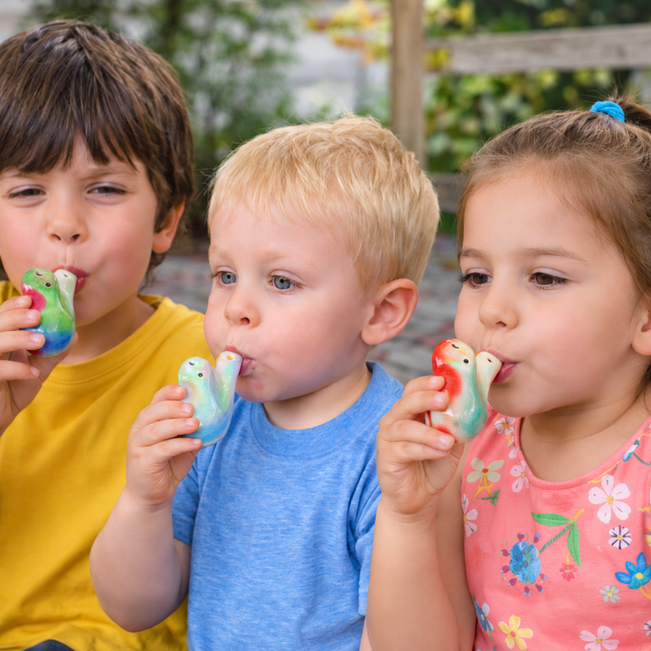 Three children blowing colorful bird-shaped whistles outdoors
