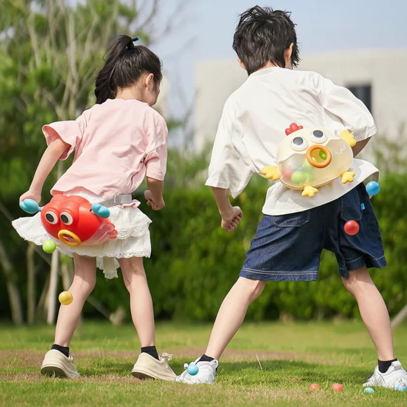 Two children playing outdoors with crab and chick ball games strapped around their waists