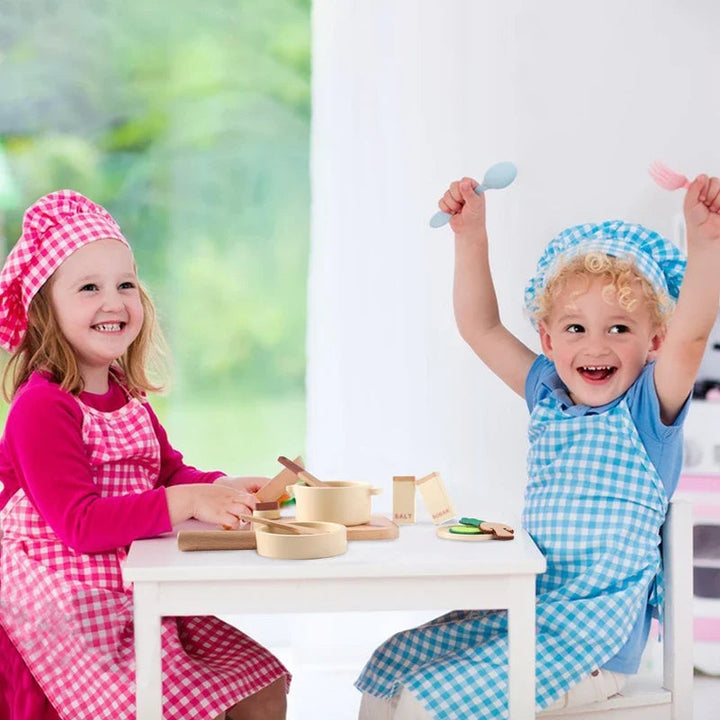 Two children in chef hats and aprons playing with wooden cookware at a small table