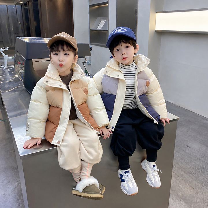 Two children seated in cream color-block winter coats, one with rust panels and one with navy panels.