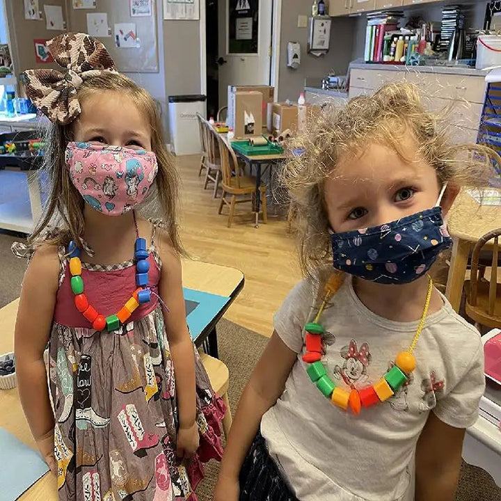 Two children wearing necklaces made from colorful lacing beads