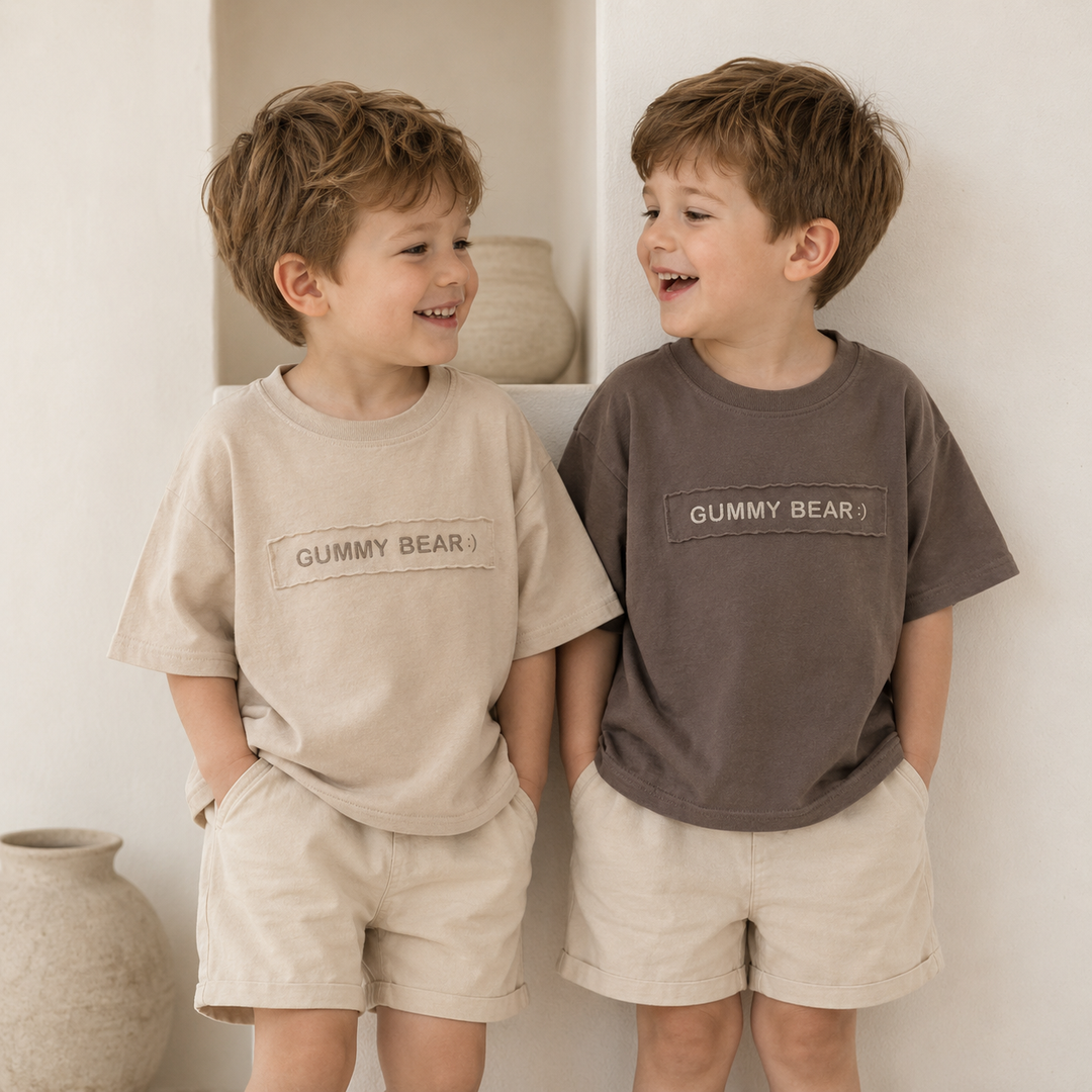Two children wearing beige and brown Gummy Bear T-shirts with light-colored shorts